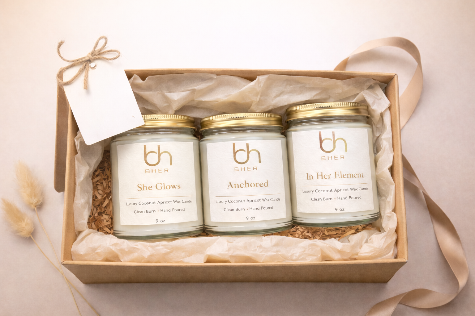 Luxury BHER candle gift set featuring three coconut apricot wax candles—She Glows, Anchored, and In Her Element—arranged in a natural gift box with tissue paper and ribbon.
