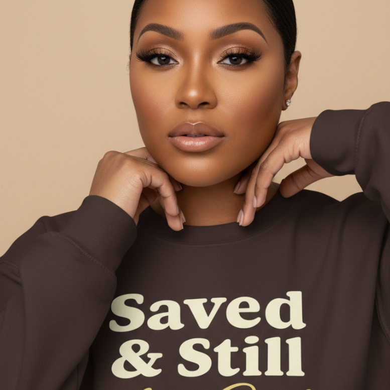 Woman wearing a brown sweatshirt with 'Saved & Still that Girl' text on a beige background