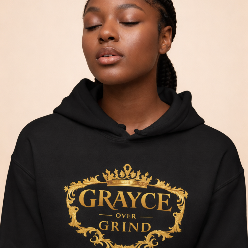 Model wearing a black “Grayce Over Grind” hoodie with gold detailing, photographed against a soft neutral background
